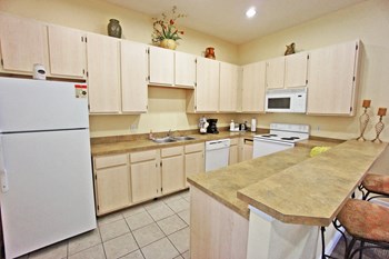 Clubhouse Kitchen with beige cabinets, white appliances, and breakfast bar and bar stools